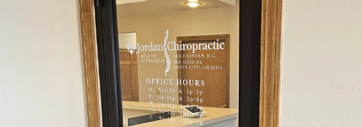 A glass door entrance to a clinic with visible office hours and a welcome mat.
